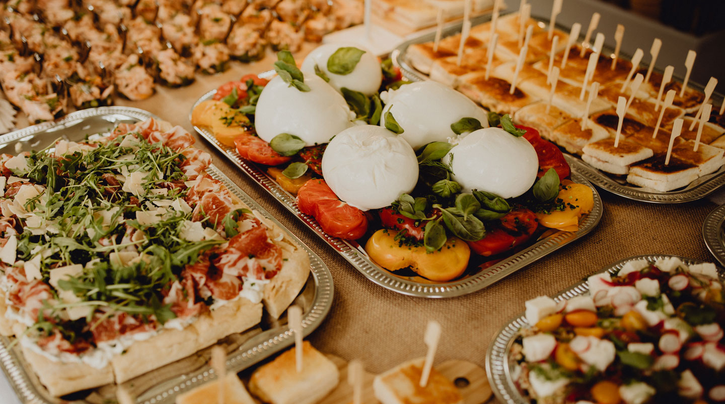 Plateau professionnel présentant une vingtaine de pièces cocktail variées incluant verrines salées, mini-brochettes, toasts garnis et bouchées chaudes, disposition soignée sur ardoise avec fond événementiel flou